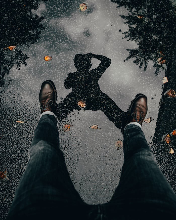 Artistic reflection of a man standing in a puddle with fallen leaves.